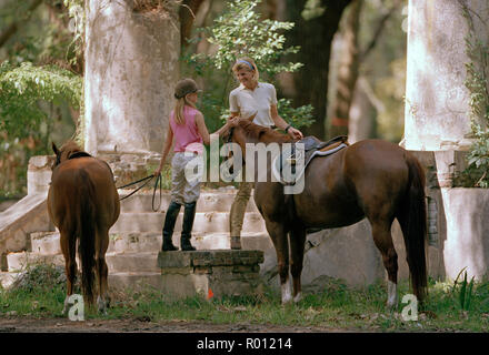Teenage girl standing with her mid-adult mother and two horses. Stock Photo