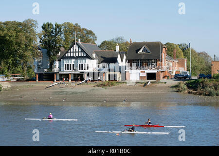 rowers on the river thames close to chiswick bridge, with the boathouse of the mortlake anglian and alpha boat club in background Stock Photo