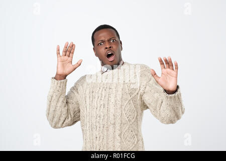 African man looking scared as noticing ghost tilting backwards and raising hands in surrender being terrified Stock Photo