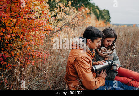 Woman pours hot tea out of thermos in autumn forest. Couple in love having drinks outdoors Stock Photo