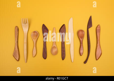 Handcrafted wooden utensils on yellow background. Fork, spoons and knives. Stock Photo