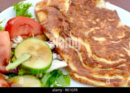 Golden cooked omelette with side salad served on a white plate Stock Photo