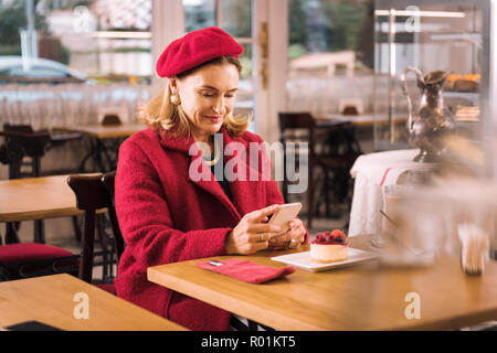 Stylish mature lady wearing red coat sitting in cozy cafe Stock Photo