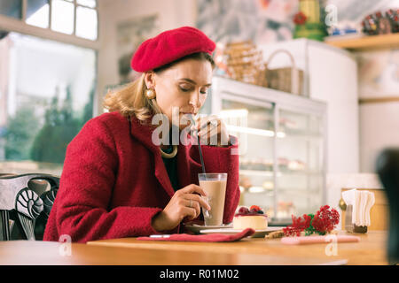 French woman wearing red outfit drinking latte sitting in nice bakery Stock Photo