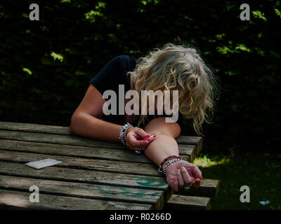 A woman injecting drug into her arm with a syringe in the street and a dose of drug to the side Stock Photo