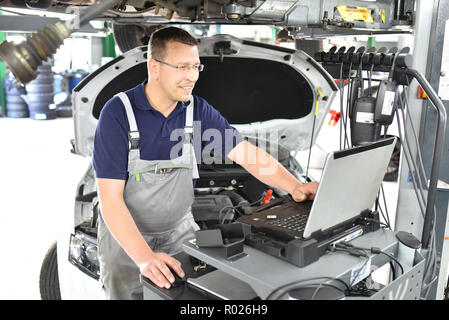 car mechanic maintains a vehicle with the help of a diagnostic computer - modern technology in the car repair shop Stock Photo