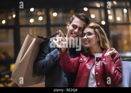 Beautiful couple with shopping bags is talking and smiling while doing shopping in the mall focus on the woman Stock Photo
