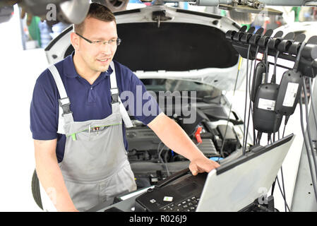 car mechanic maintains a vehicle with the help of a diagnostic computer - modern technology in the car repair shop Stock Photo