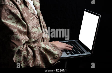 US Army. Young soldier working with a laptop computer with blank screen on black background Stock Photo