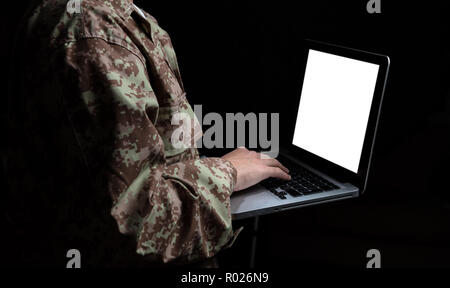 US Army. Young soldier working with a laptop computer with blank screen on black background Stock Photo