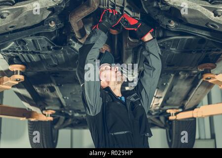 Car Mechanic Undercarriage Maintenance. Caucasian Worker Adjusting Tension on a Vehicle Drivetrain Elements. Stock Photo