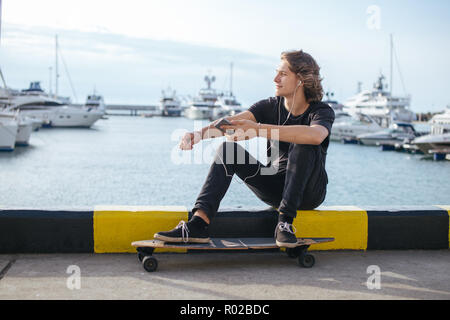 hipster man sitting on longboard using his phone Stock Photo