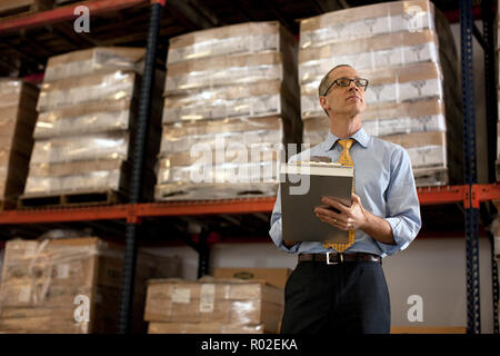 Thoughtful businessman taking notes on a clipboard in a warehouse. Stock Photo