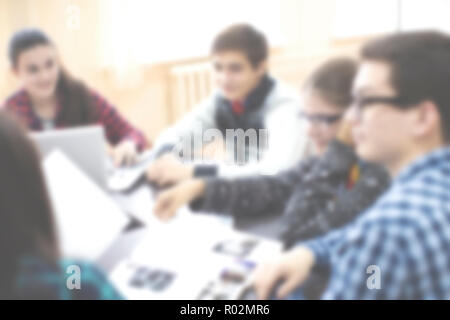 Students sitting together at table using laptop in class Blured Stock Photo