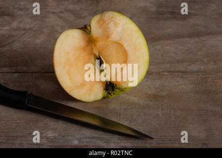 Bramley apple cut in half and slightly oxidising with internal structure fluorescence and unseen colours from blacklight and pigments in wooden board Stock Photo