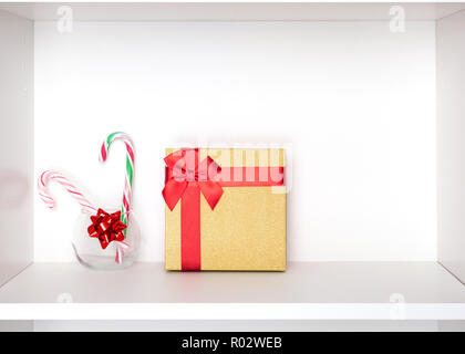 Christmas gift with candy canes on white cabinet shelf. Holiday preparations. Copy space Stock Photo