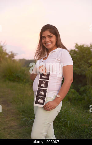Hispanic pregnant woman with ultrasound print on outdoor background Stock Photo