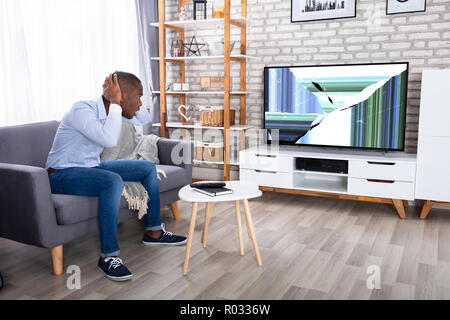 African Man Sitting On Couch Looking At Broken TV Stock Photo