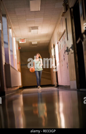 Teenage girl dribbling basketball in school corridor Stock Photo