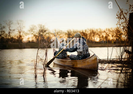 Portrait of a young adult man and his wife sitting in a canoe wearing camouflage attire on a lake. Stock Photo