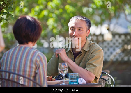 Smiling mid-adult man sitting at an outdoor table in a restaurant with a woman. Stock Photo