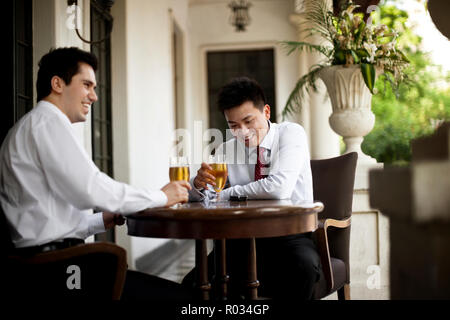 Two smiling businessmen sharing a drink at a table on the balcony of a restaurant. Stock Photo