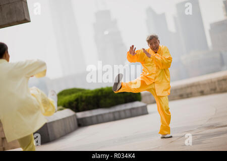 Senior man wearing traditional clothing and practicing martial arts in a courtyard in the city. Stock Photo