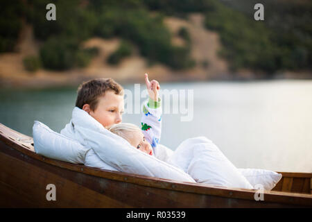 Boy and his young brother wrapped in a rug while sitting inside a wooden boat. Stock Photo