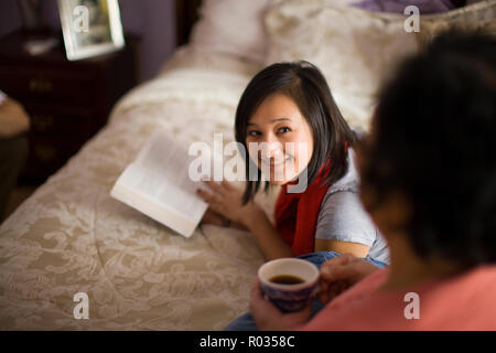 Teenage girl reading in her bedroom and talking to her mom Stock Photo