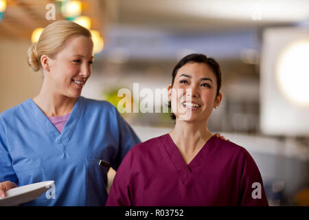 Smiling young nurses puts her arm around her colleague as they wait in line to get their lunch from the hospital canteen. Stock Photo
