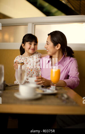 Smiling middle-aged mother and her young daughter enjoy eating breakfast together at a cafe. Stock Photo