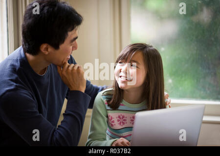 Father and daughter smile while working on a laptop together. Stock Photo