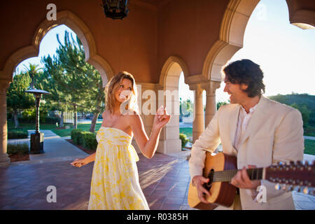 Smiling mid adult man playing an acoustic guitar while his partner looks on. Stock Photo