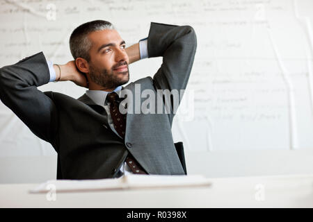 Businessman sits relaxed at desk with hands behind his head. Stock Photo