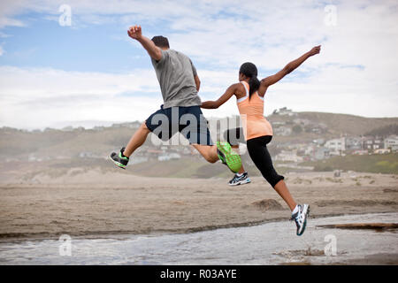 Young couple jumping over shallow water on a beach. Stock Photo