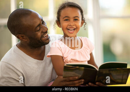 Smiling father and daughter reading a book together. Stock Photo