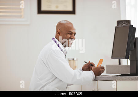 Laughing male doctor holding a box of medication inside his office. Stock Photo