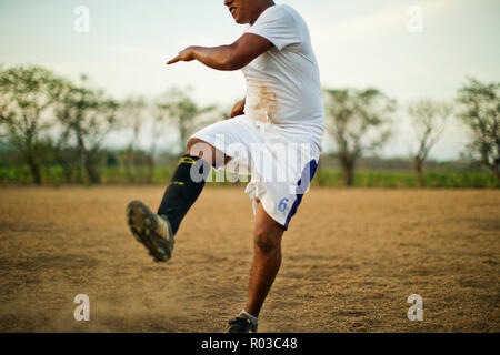 Young soccer player kicking his leg in the air while playing on a dusty soccer field. Stock Photo