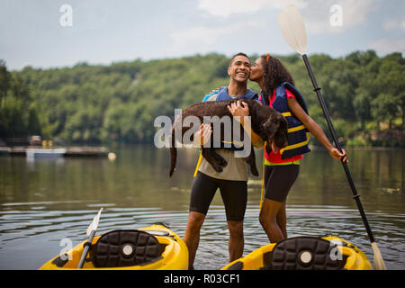 Young kayaker kissing her boyfriend's cheek while he holds a dog. Stock Photo