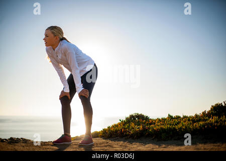 Young woman takes a break from her sunrise jog along the cliffs to admire the view of the ocean. Stock Photo
