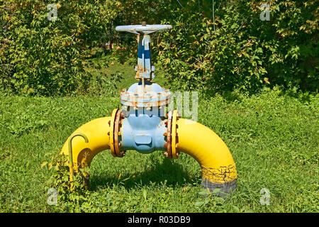 Large gas pipe with a valve and flanges above the ground on against the nature background Stock Photo