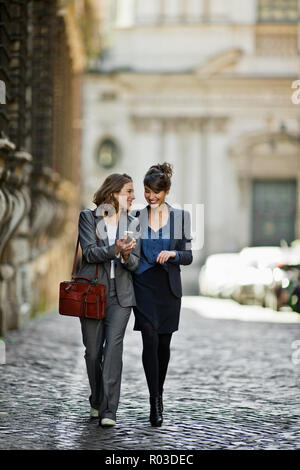 Two young women happily stroll at chat on the way home from the office. Stock Photo
