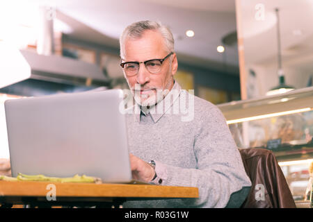 Handsome mature man wearing grey sweater working hard using his laptop Stock Photo