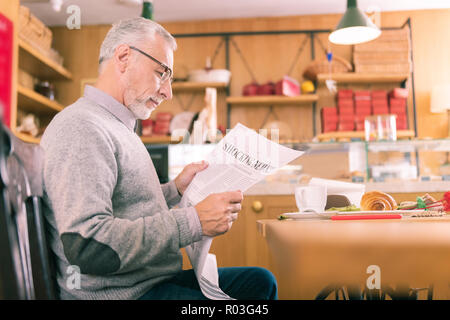 Mature grey-haired man feeling involved in reading local newspaper Stock Photo