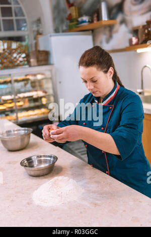 Dark-haired baker adding egg to flour while preparing dough Stock Photo