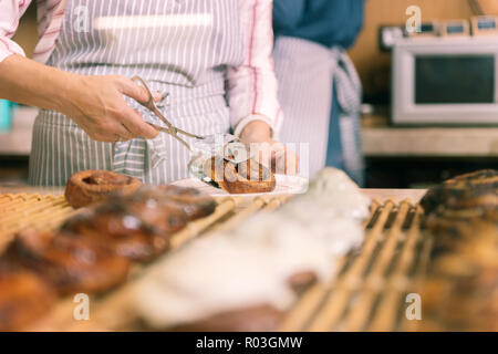Woman working in bakery putting nice cinnamon bun on plate Stock Photo