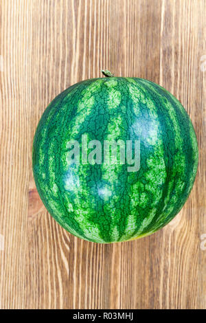 one watermelon with green color with stripes on the peel, lie on a wooden table Stock Photo