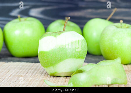 peeled green ripe apple lying on a cutting board with whole apples in the skin Stock Photo