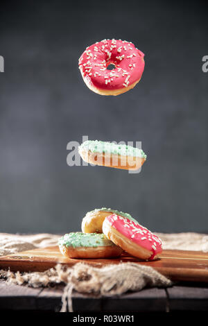 Donuts with pink and green icing with sprinkles over rustic table. Vertical orientation of photo. Stock Photo