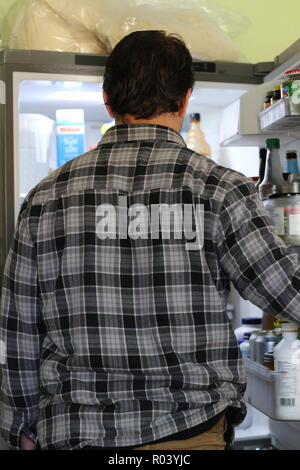 Rear View Of A Confused Young Man Looking At Food In Refrigerator. Stock Photo